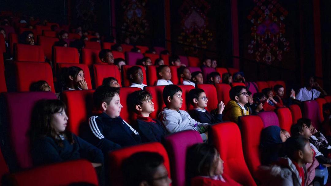 A large group of children are seated in a cinema, watching a film.