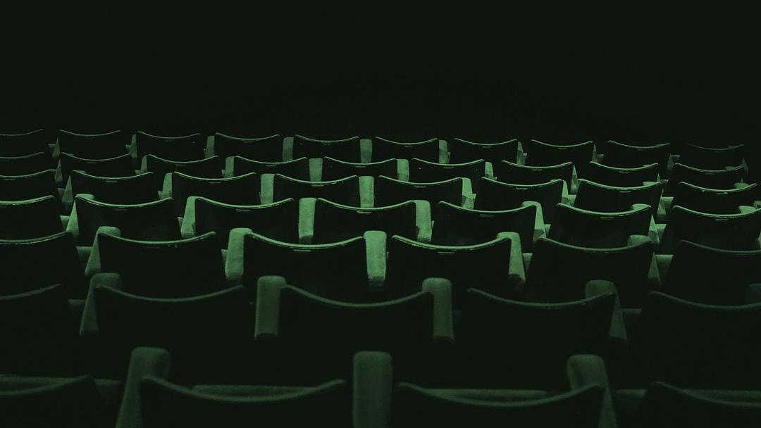 An empty movie theatre with rows of plush dark green seats facing away from viewer.
