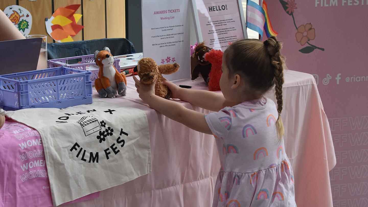 A young girl interacts with stuffed animals at a table displaying 