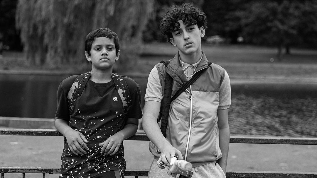 Two boys stand by a railing next to a body of water in a black and white image, looking directly at the camera.