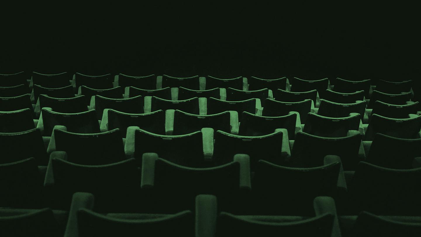 An empty movie theatre with rows of plush dark green seats facing away from viewer.