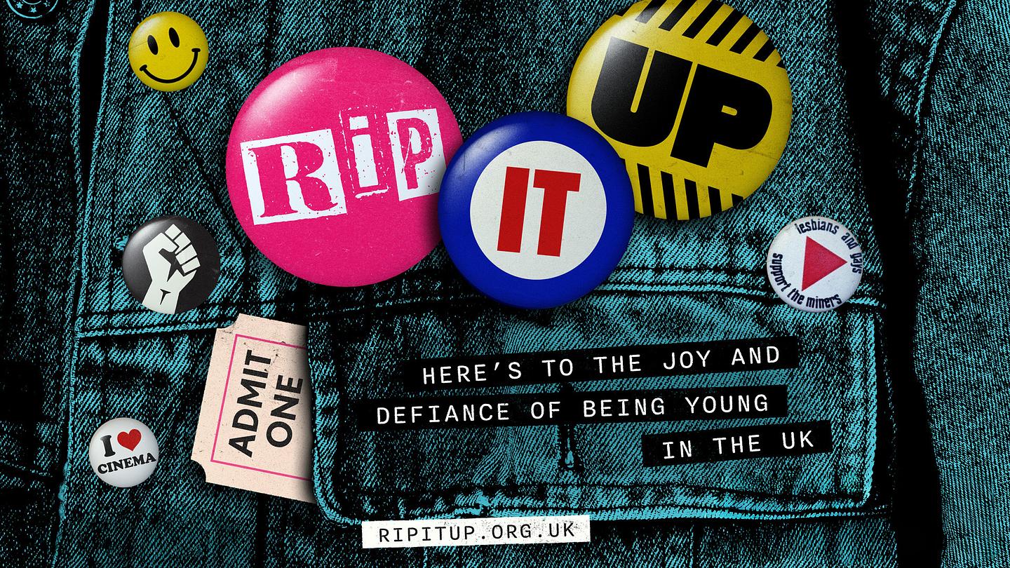 A close-up shot of a denim jacket adorned with various pin badges and tickets spelling ‘RIP IT UP’. Text reads ‘Here’s to the joy and defiance of being young in the UK’, and ‘ripitup.org.uk’. 