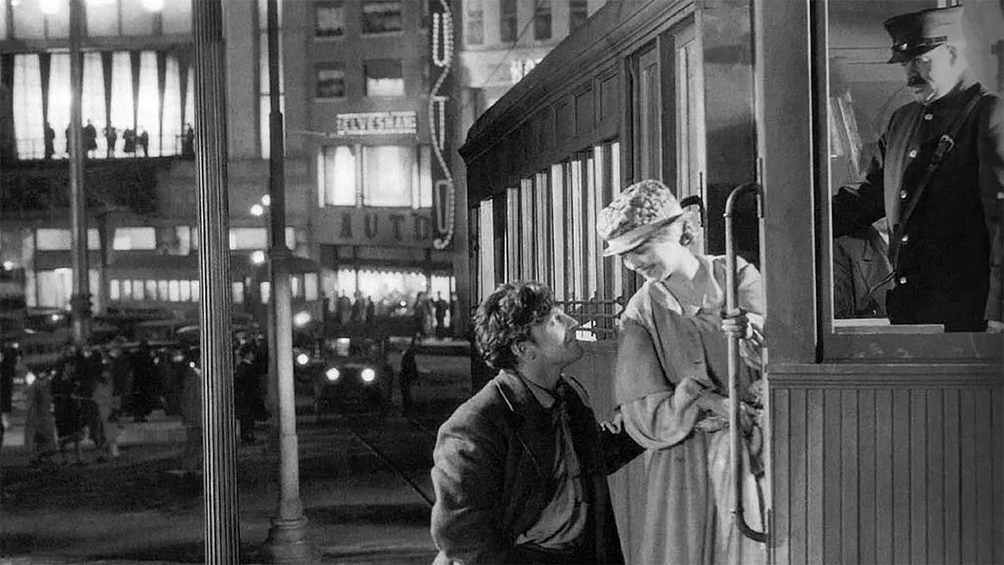 Still from Sunrise shows a man and woman next to a trolley car, with city buildings and lights in the background.