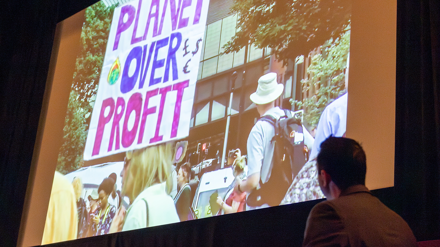 Projection of a climate demonstration on a large screen, featuring a hand-held sign reading 