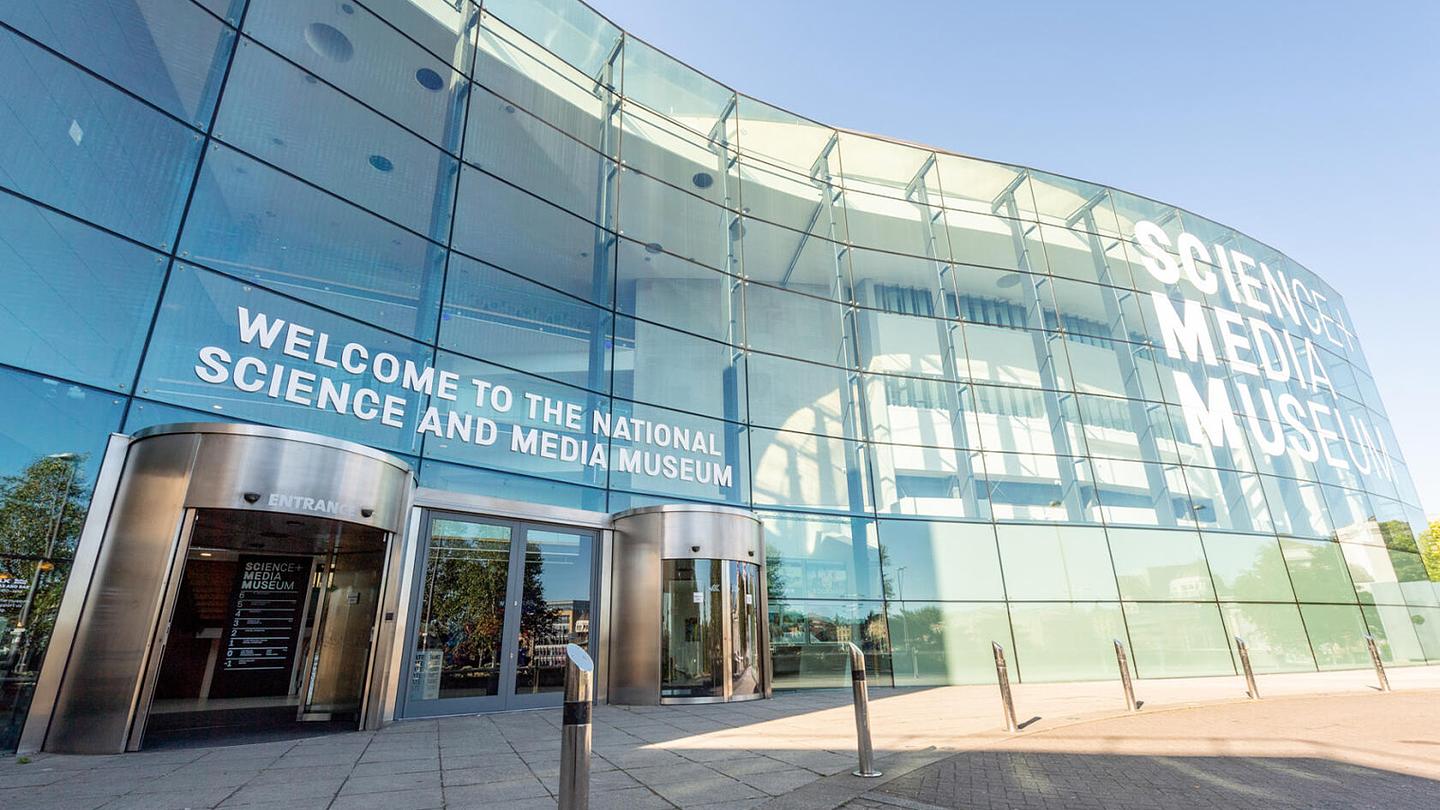 Exterior photograph of the National Science and Media Museum in Bradford.  The building is modern with a curved glass façade and the museum's name is displayed in large, white lettering. 