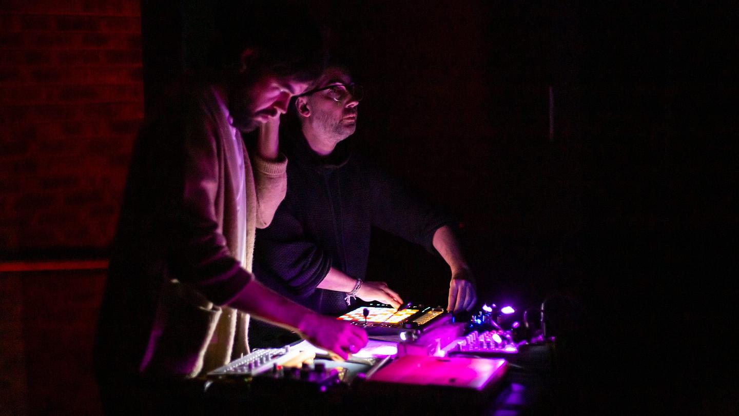 Two technicians operate equipment in a dimly lit setting with red and purple lights.