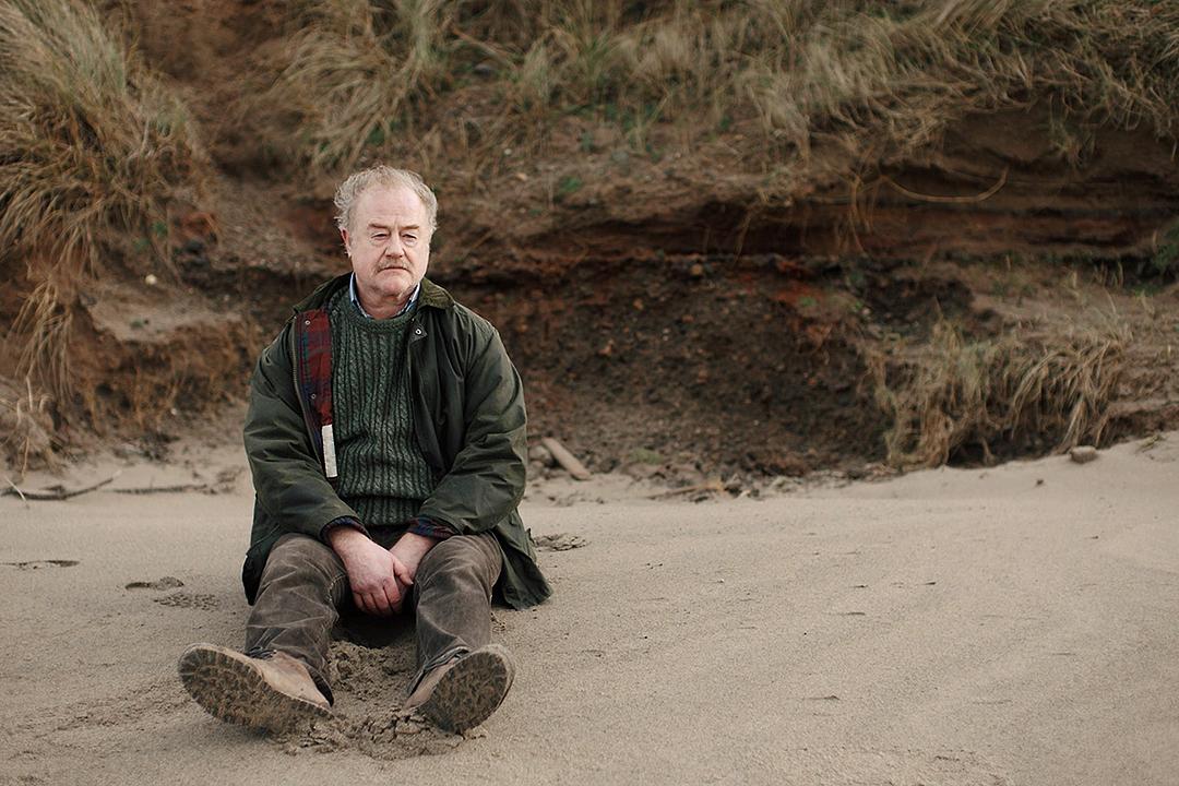 Glenn sits on the beach looking out at the sea in a scene from SALT WATER TOWN