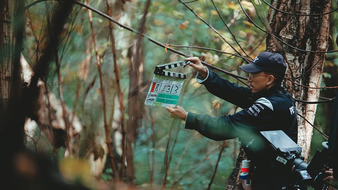 Behind the scenes still from Predators - man wearing cap holds a clapperboard in a forest scene