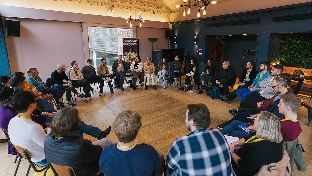 A group of people sit in a circle on chairs in an indoor space, engaged in discussion.