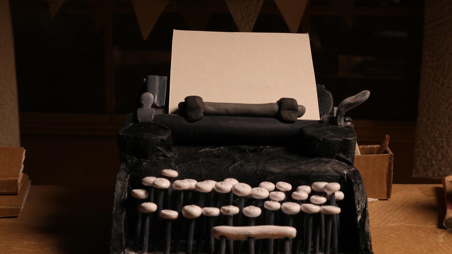 Still from Type (2021) features a clay model of a black typewriter, with rounded, white keys and a blank piece of white paper inserted.