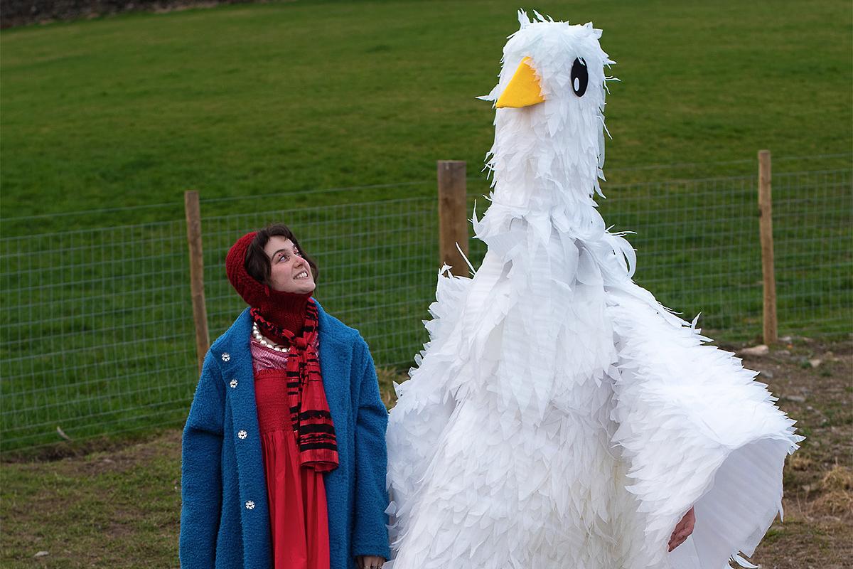 Chicken Girl smiles at a giant chicken in a scene from CHICKEN GIRL