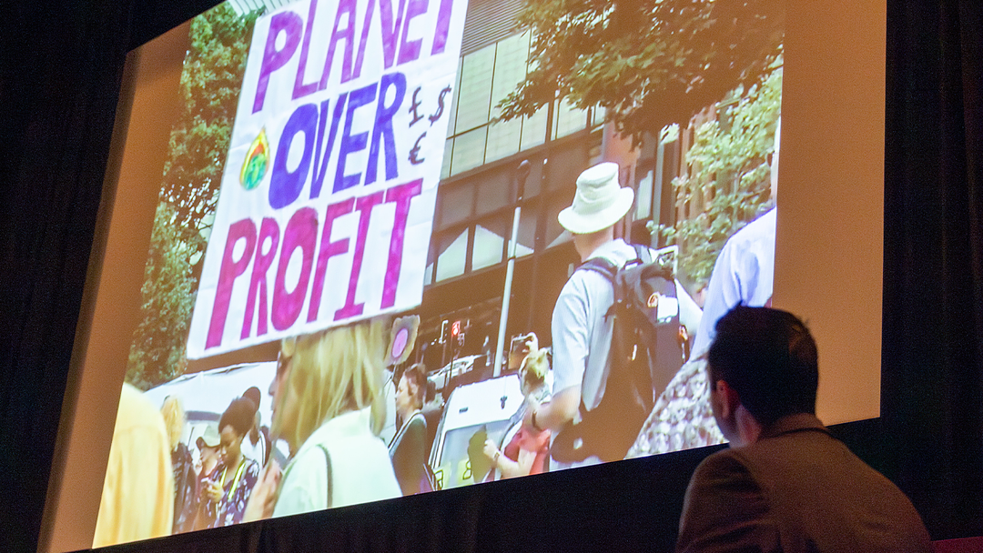 Projection of a climate demonstration on a large screen, featuring a hand-held sign reading 