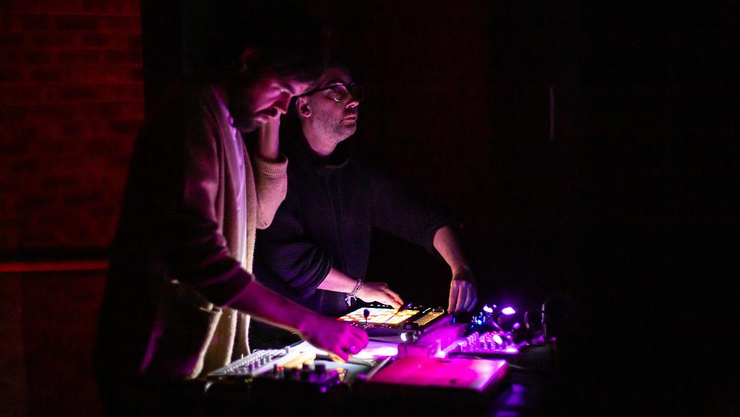 Two technicians operate equipment in a dimly lit setting with red and purple lights.