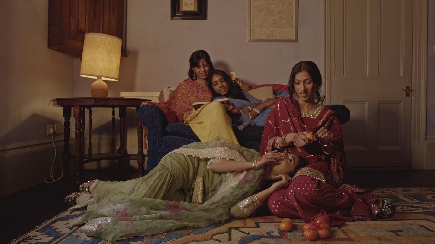 Still from Char Bahnien features four women, dressed in colourful Pakistani clothing, relaxing together in an intimate living room scene.