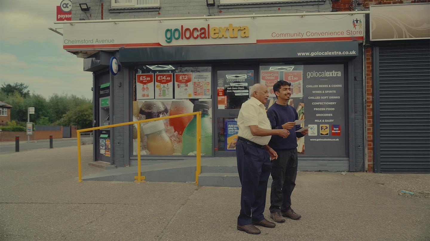 Still from Shop Dada: Darshan and his grandfather stand outside a convenience store, engaged in conversation.