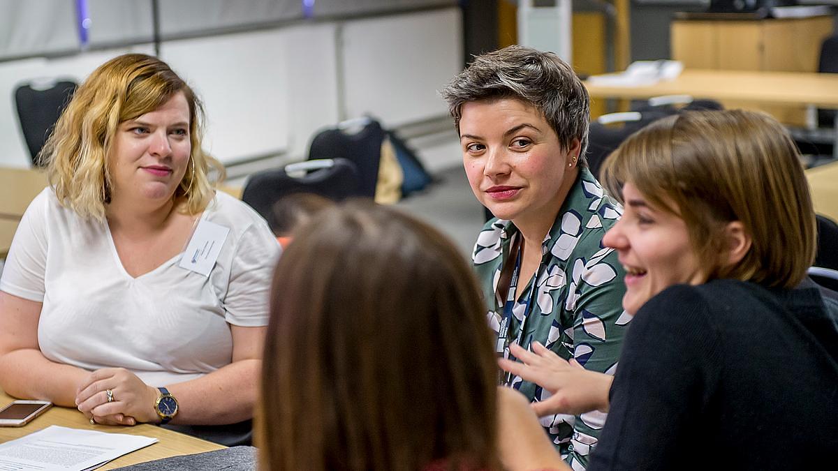 A group of people sits at a table indoors, engaging in conversation and smiling.