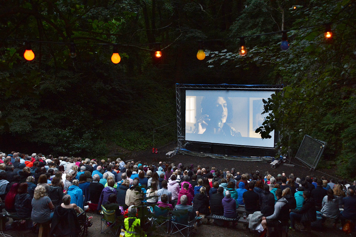 A group of people watching a film at an outdoor cinema surrounded by trees